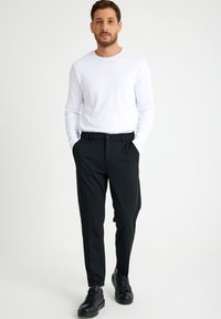 Zwarte broek met een platte voorkant, een klassieke pasvorm en riemlussen, gecombineerd met een strakke witte overhemd met lange mouwen en zwarte sneakers.