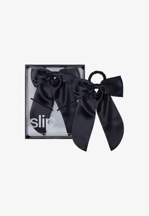 Accessoires en soie noire pour les cheveux dans une boîte, comprenant deux grands nœuds et un élastique. Texture lisse avec une finition brillante.