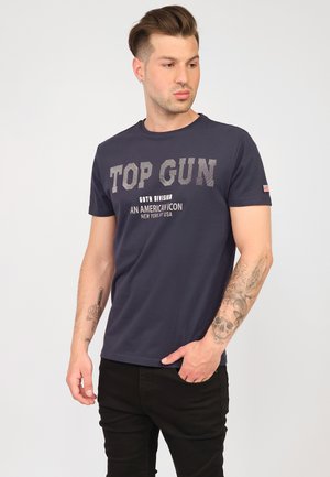 Mörkblå T-shirt i bomull med en grafisk "TOP GUN" tryck i ljusgrått och svart, med korta ärmar och rundad hals.