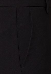 Mustat juhlahousut, joissa on sileä pinta, suora leikkaus ja sivutaskut, valmistettu kevyestä kankaasta ja istuu räätälöidysti.