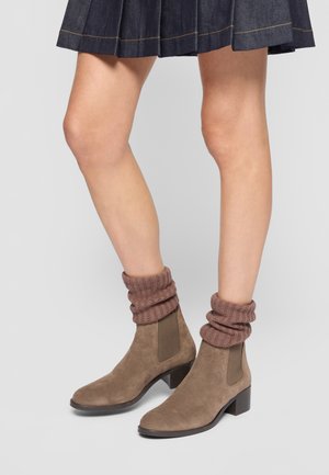 Bottines en daim marron avec un revers en tricot élastique marron, un petit talon carré et des panneaux élastiques sur les côtés. La jupe a une texture en denim et une couleur sombre.