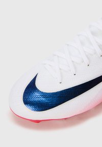 Witte sportschoen met witte veters en een grote blauwe Nike swoosh op de bovenste voorkant, met een glimp van een rode zool eronder.