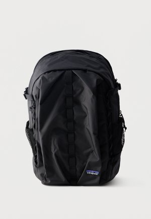 Czarny plecak Patagonia z pionowym paskiem z przodu, bocznymi kieszeniami z siateczki i górną komorą zapinaną na zamek, na jednolitym białym tle.
