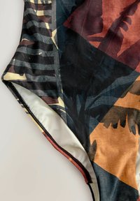 Maillot de bain une pièce avec un motif abstrait multicolore, présentant des tons sombres et chauds, une texture lisse et des bords surpiqués contrastants.