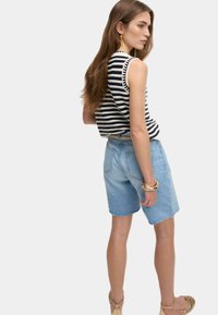 Top sans manches rayé avec dentelle, associé à un short en denim bleu clair. Détails supplémentaires : bracelets dorés et sandales à lanières.
