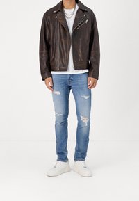 Ruskea nahkainen biker-takki hopeisilla vetoketjuilla, yhdistetty revittyihin vaaleansinisiin farkkuihin ja valkoisiin lenkkareihin. Moderni istuvuus ja rento tyyli.