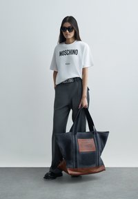 Μαύρη και γκρι τσάντα tote με δερμάτινες λεπτομέρειες, χαρακτηριστική υφή, μεγάλο μέγεθος και λογότυπο στην μπροστινή πλευρά.