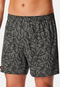 Shorts de boxe gris foncé avec un motif de feuilles noires, taille élastique, fermeture à boutons et une texture douce et légère en mélange de coton.