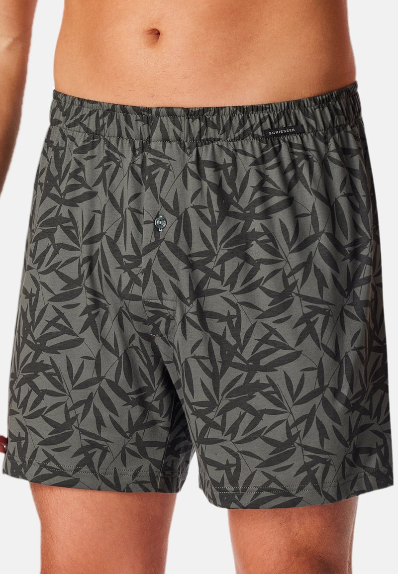 Shorts de boxe gris foncé avec un motif de feuilles noires, taille élastique, fermeture à boutons et une texture douce et légère en mélange de coton.