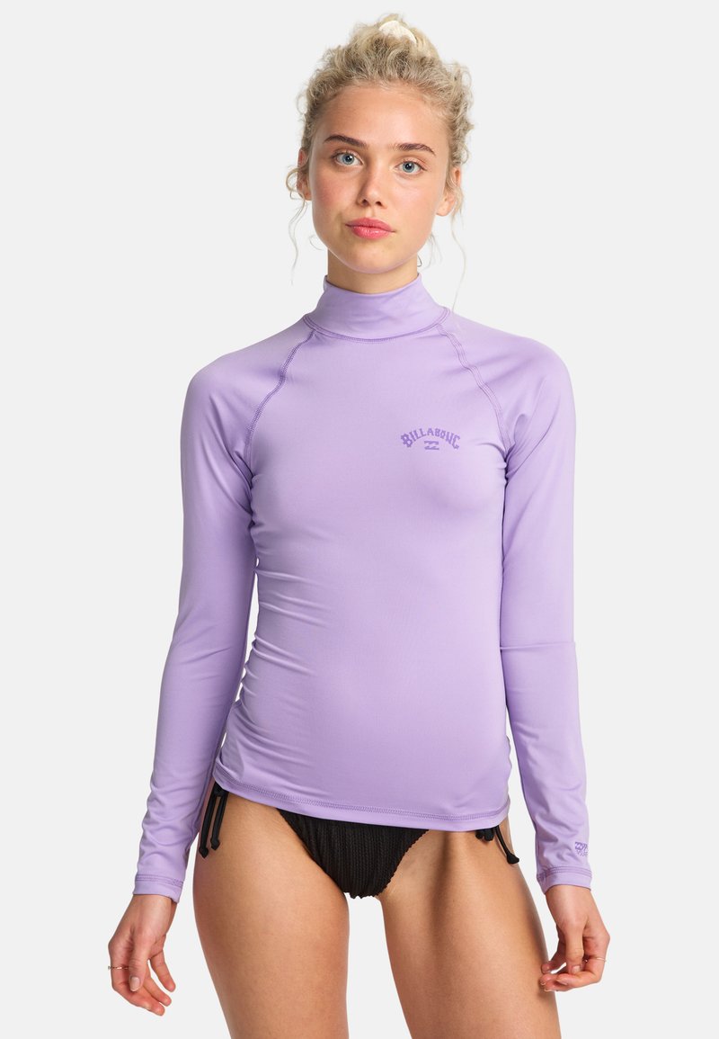 Il rash guard a maniche lunghe di colore lavanda presenta un colletto alto e un dettaglio con il logo. Abbinato a un costume da bagno nero con texture, evidenziando una silhouette aderente.