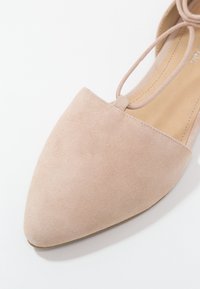 Scarpa piatta nuda in suede con punta appuntita; presenta una sottile cinghia alla caviglia e una fodera interna liscia. La texture è morbida e il colore è uniforme.