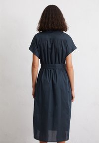 Abito blu scuro fino al ginocchio realizzato in cotone. Presenta maniche corte e larghe, una schiena arricciata e una cintura legata in vita per una vestibilità regolabile.