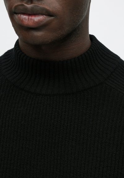 Pulover negru din tricot cu nervuri, cu un guler înalt și texturat. Materialul pare moale, având un design ajustat în jurul gâtului.