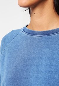 Blå bomullssweatshirt med rundad hals, med en mjuk textur och raglanärmar, som har en blekt och något sliten finish.