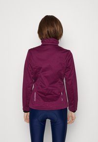 Lila Sportjacke mit hohem Kragen, strukturiertem Stoff, figurbetontem Schnitt und zwei seitlichen Reißverschlusstaschen.