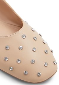 Beige kožená bota s špičatou špičkou, ozdobená stříbrnými hroty a kamínky uspořádanými rovnoměrně. Hladký povrch, nízký střih.