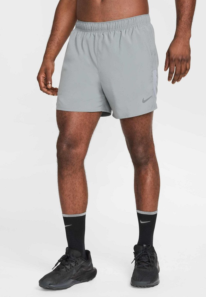 Grå atletiska shorts med elastisk midja och sidofickor, med en diskret Nike-logotyp. Bärs med svarta skor och strumpor.