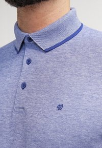Modrá polokošile s texturovaným límcem, malým vyšitým logem, knoflíkovou légou a melírovanou úpravou.