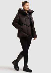 Puffy black jacket with a high collar, featuring diamond quilted design. Worn over black leggings and knee-high black boots.