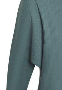 Nahaufnahme von türkisfarbenem geripptem Strickstoff mit diagonalen und vertikalen strukturierten Mustern auf einem Kleidungsärmel.