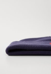 Berretto a maglia blu navy, ripiegato, che mostra un tessuto texturizzato e un piccolo accento rosso. Materiale morbido con un design aderente, ideale per il freddo.