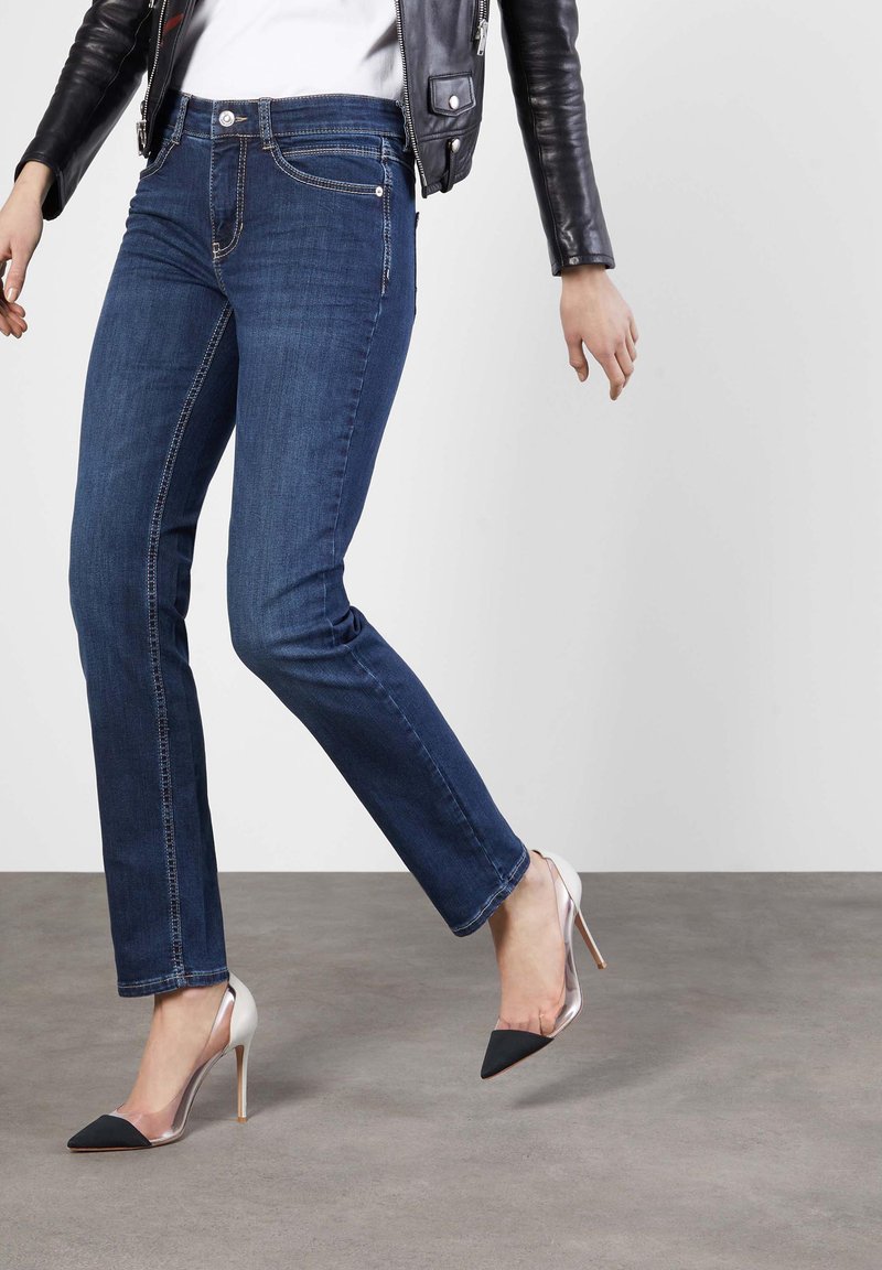 Vaqueros de denim azul oscuro con corte slim, que cuentan con un diseño clásico de cinco bolsillos y costuras ligeras. Combinados con unos zapatos de tacón transparente.