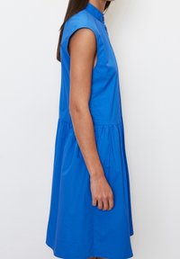 Abito senza maniche blu con colletto abbottonato, corpetto aderente e gonna arricciata. Realizzato in tessuto liscio, presenta una silhouette pulita.