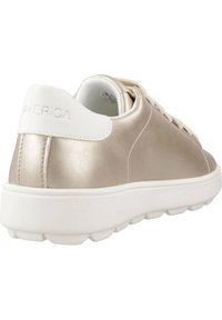 Zapatilla metálica dorada con acento blanco en el talón y cordones. Presenta una textura suave, puntera redonda y una suela de goma con patrones de tracción.