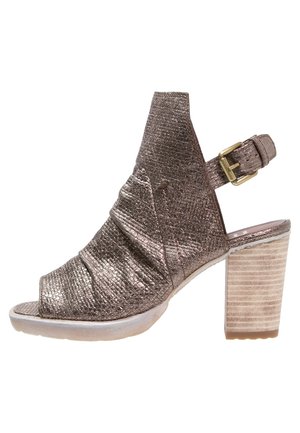 Metallic bronze open-toe shoe with a wrinkled texture, ankle strap, and a block heel featuring a striped wood-like pattern.