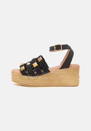 Zwarte gevlochten sleehak sandaal met gouden studs, enkelriem en een met jute omwikkelde hak. Heeft een gestructureerd bovenwerk en een gevoerde binnenzool.