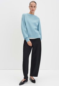 Pull bleu clair à col bateau, à manches longues et en tissu texturé. Associé à un pantalon large noir et des chaussures plates.