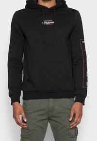 Felpa nera in cotone con tasca frontale e cappuccio con cordoncino. Presenta testo bianco e rosa sul petto e sulla manica. Polsini e orlo a coste.