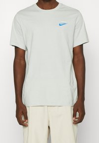 Light grey cotton t-shirt with short sleeves, round neckline. Features a small blue Nike logo on the upper left chest area.