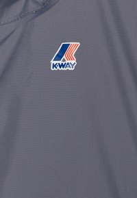 Tessuto leggero grigio con una sottile trama; presenta un logo K-Way in blu, rosso e bianco. Gli accenti sono minimi e moderni.