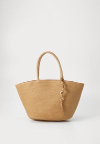 Woven straw tote bag v bežni barvi, ki ima dve okrogli ročki in detajl s frufruji ter školjkami. Široka osnova in odprt zgornji del.