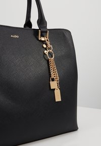 Borsa a spalla nera realizzata in materiale testurizzato, con hardware dorato, un accento a catena e un piccolo lucchetto decorativo. Logo del marchio visibile.