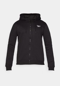 Črna zip-up kapuca iz mehkega blaga, ki ima kapuco na vrvico in rebraste manšete. Opazen logo Reebok na levi strani prsnega koša.