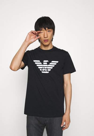 Black cotton t-shirt featuring a white stylized eagle logo with horizontal stripes. The design is modern, with short sleeves and a crew neckline.