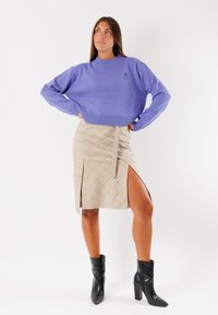 Maglione viola lavorato a maglia con orlo a costine, abbinato a una gonna a quadri beige con uno spacco laterale. Stivali neri alla caviglia completano l'outfit.