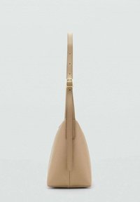 Bolso de mano de cuero beige con forma triangular, una correa larga y ajustable, y una textura suave. Presenta una hebilla dorada cerca de la parte superior.