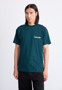 Dunkelgrünes Baumwoll-T-Shirt mit Rundhalsausschnitt und kurzen Ärmeln, mit einem sandfarbenen Logodesign auf der linken Brust.