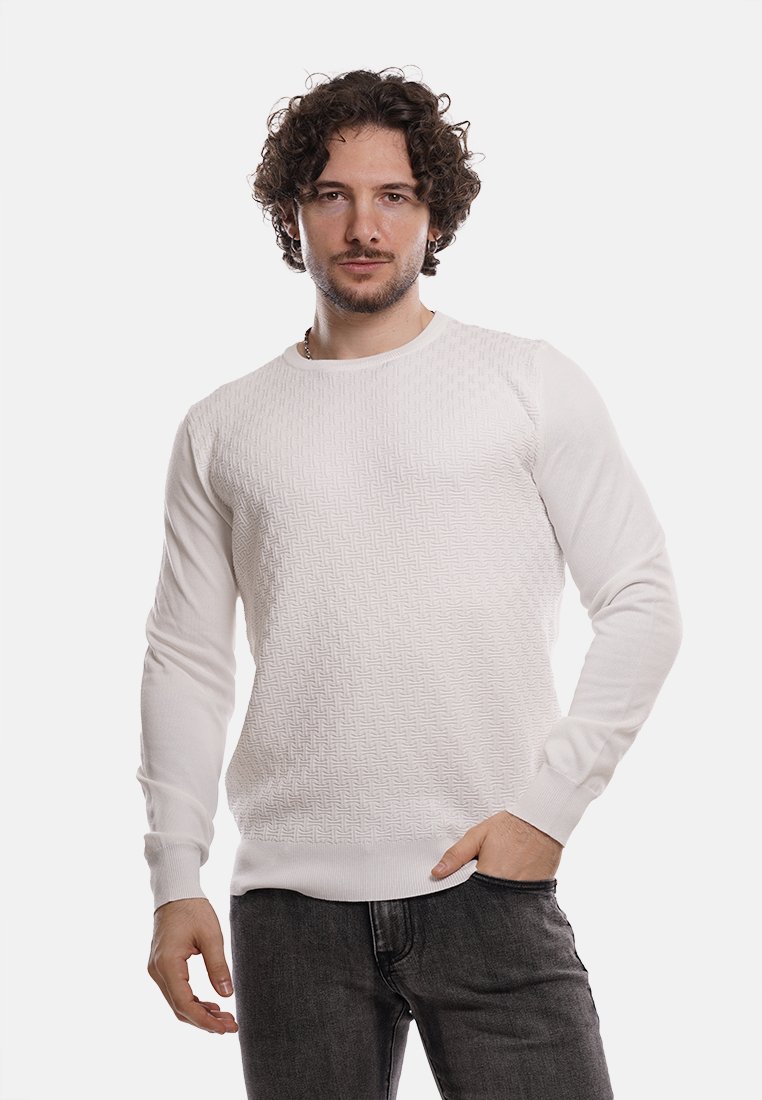 Maglione bianco a maglia con motivo testurizzato sul davanti, polsini e orlo a coste. Abbinato a jeans scuri. Il modello si trova davanti a uno sfondo semplice.