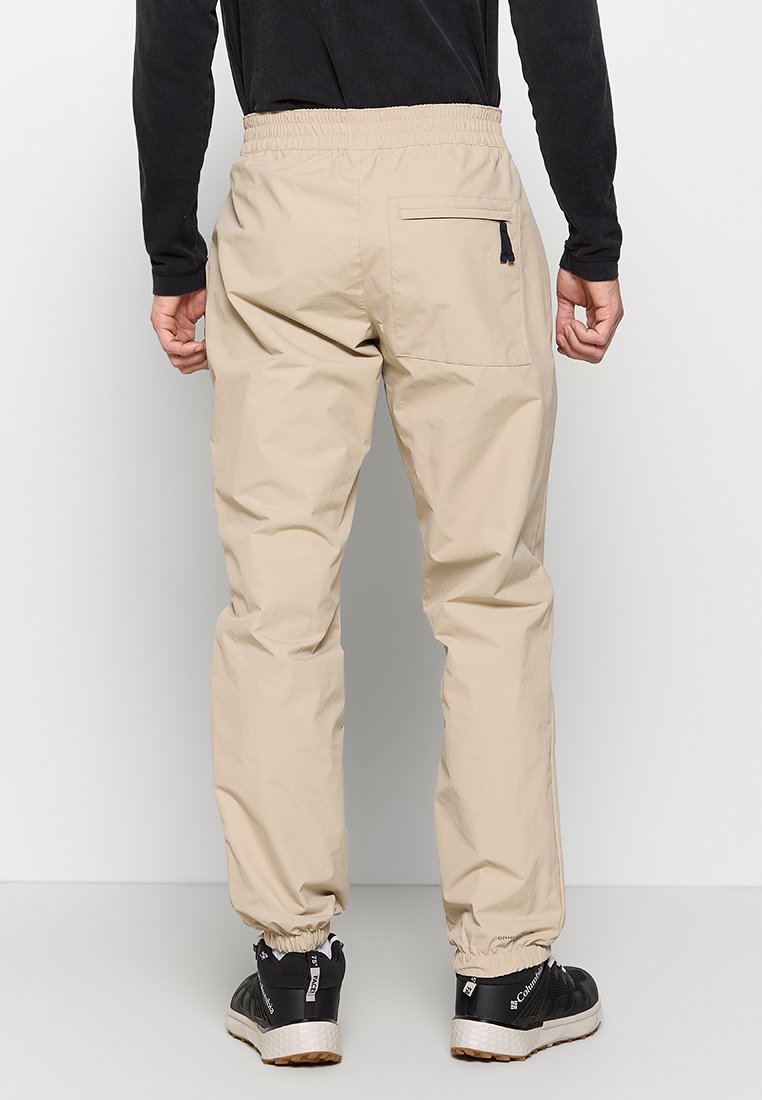 Pantalons en nylon beige avec taille élastique et chevilles resserrées, dotés d'une poche arrière zippée et de détails de couture minimaux.