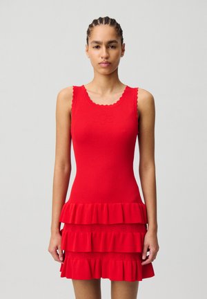 Robe rouge à côtes avec encolure festonnée, corsage ajusté et jupe à volants superposés ornée de détails en œillets le long des couches.