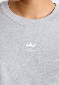 Felpa grigia in misto cotone, con girocollo e logo Adidas bianco con tre strisce sopra una grafica a tre foglie.