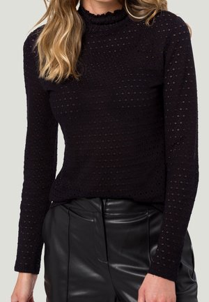 Top nero a maniche lunghe con un motivo testurizzato a pois e un collo alto arricciato, abbinato a pantaloni di pelle nera.