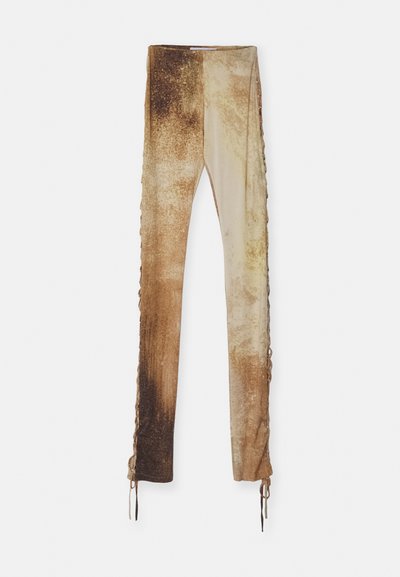 Leggings dégradés marron avec une finition texturée, dotés de lacets sur les côtés, d'une coupe ajustée et de teintes variées allant du beige clair au brun foncé.