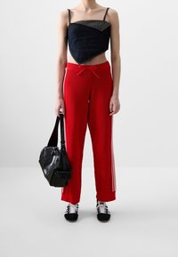 Lyhyt denim-toppi kolmion muotoisella kuviolla, punaiset neulehousut sivuviivoilla, musta olkalaukku ja musta-valkoiset tennarit.