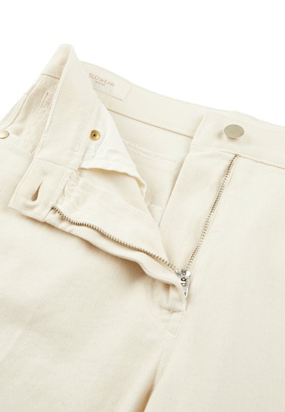 Pantaloni in cotone beige con zip e chiusura a bottone, caratterizzati da una texture a coste e un'etichetta del marchio discreta all'interno della cintura.