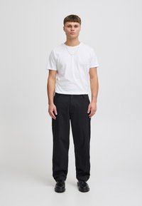 Hvit t-skjorte med rund hals, svarte bukser med avslappet passform og svarte sko. Enkel design; glatt tekstur, ingen synlige mønstre.